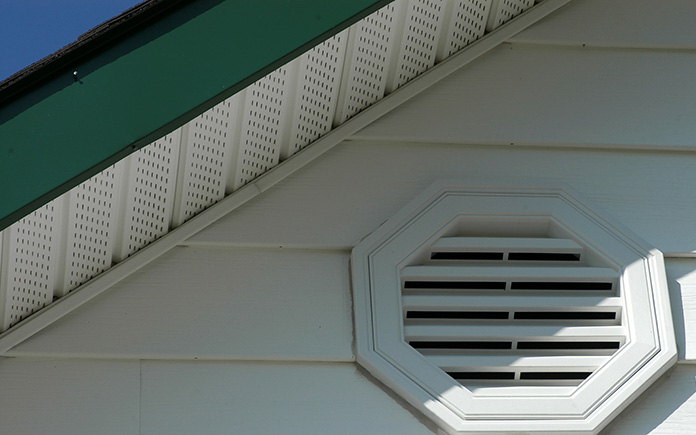 close up of white vinyl siding with air vent, soffit, and green fascia