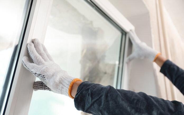 Person with gloves installing a silver framed window 
