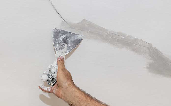 Man repairs a cracked drywall ceiling