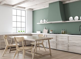 Corner of stylish kitchen with white and green walls, wooden floor, wooden countertops, dining table, and chairs, stove, and sink