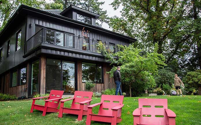Stunning Portland, Oregon house with metal roof, seen from backyard, with red lounge chairs on the grass.