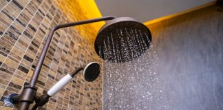 A rainfall shower head spraying water, with another shower head and tiled-bathroom walls in the background