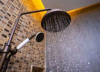 A rainfall shower head spraying water, with another shower head and tiled-bathroom walls in the background
