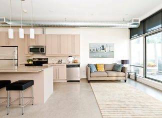 Modern condo kitchen with beige cabinets and black stools. Living room with large windows and modern couch.