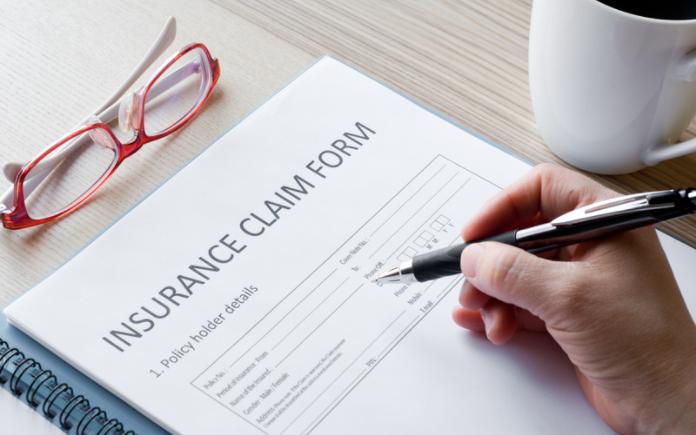 Hand holding pen over home insurance policy claim form
