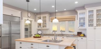 A bright kitchen with white cabinets, granite countertops, light wood floors, stainless steel appliances, and light fixtures.