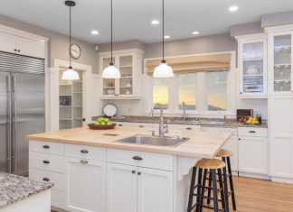 A bright kitchen with white cabinets, granite countertops, light wood floors, stainless steel appliances, and light fixtures.