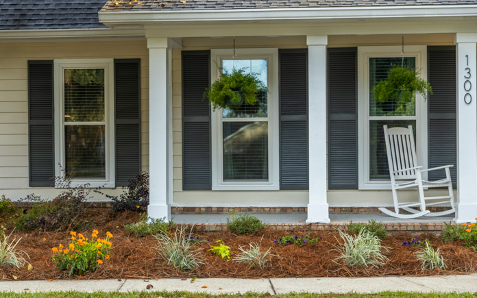 Front of a house with grey shutters, ferns and a rocking chair plus a pine-straw garden bed