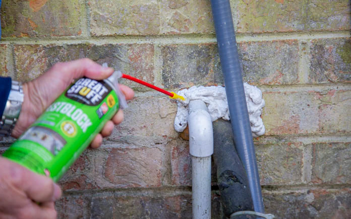 Spraying Great Stuff PestBlock into an A/C refrigerant pipe hole to block out pests for poison free rat control 