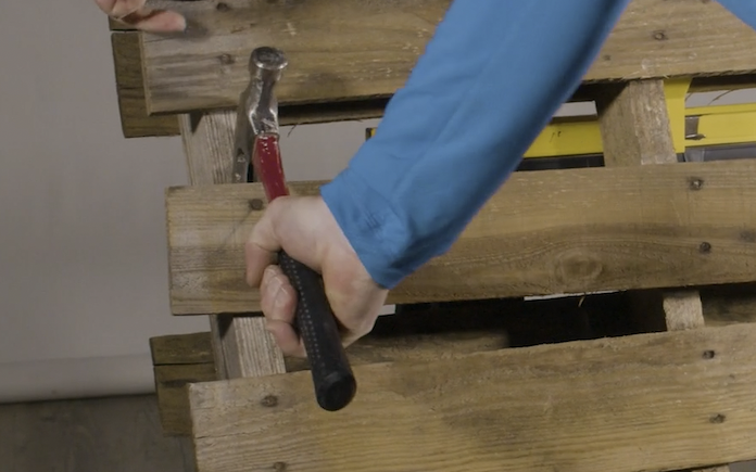 Man's hand with hammer removing wood board from pallet to make a vertical garden.