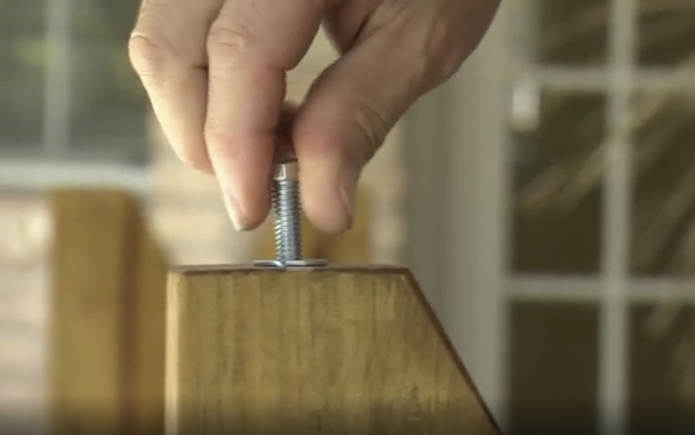Finger twisting a bolt into the bottom of a wooden leg on patio furniture
