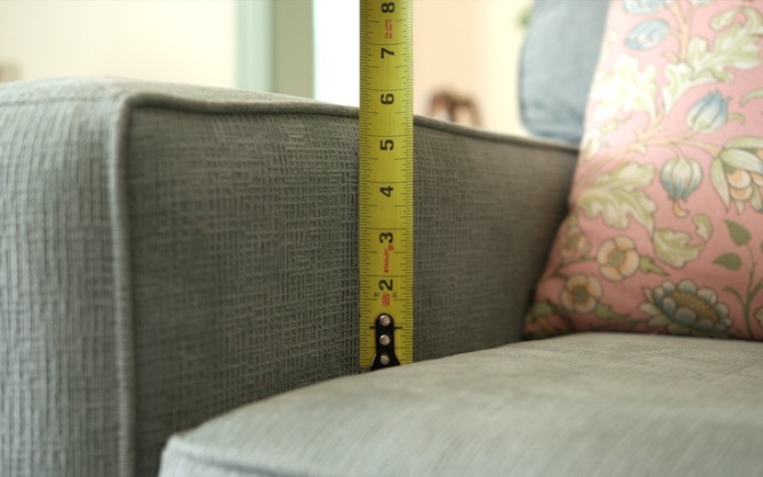Measuring a sofa arm with a tape measure.