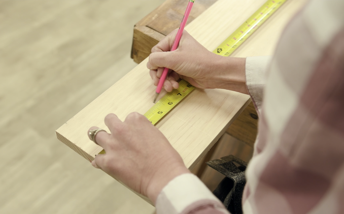 Making a pencil mark above a tape measure on a wood board.