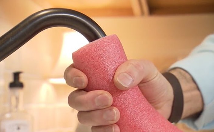 Hand holding pool noodle to kitchen water faucet.