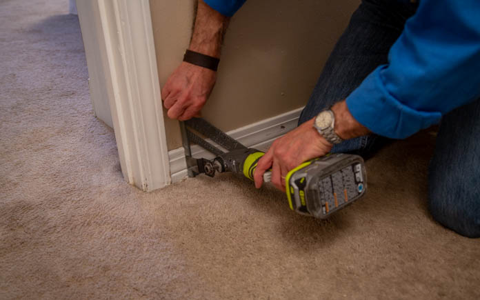 Using a speed square to line up an oscillating tool for a cut on baseboard trim 