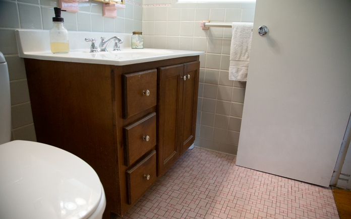 Outdated bathroom vanity next to pink tile and grey tile walls