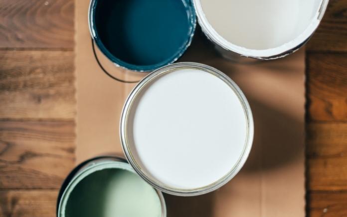 Open paint cans of white, blue and green on a wood background