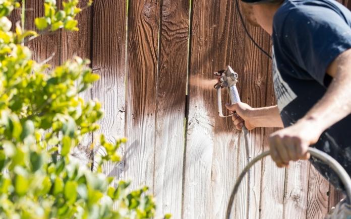 Professional painter using an airless paint sprayer to paint a fence