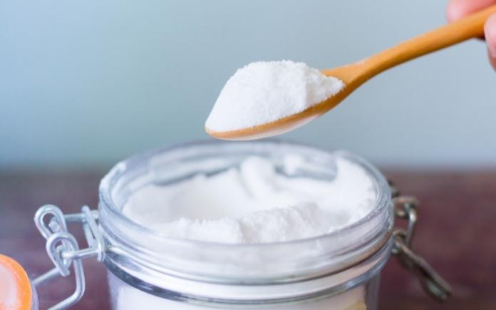 Wooden spoon scooping baking soda from a jar