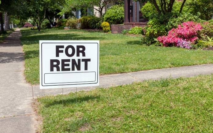 For rent sign in a front yard by a sidewalk