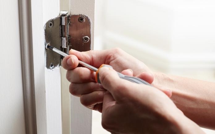 Hand using a screwdriver to adjust the door hinge