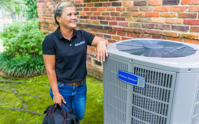 American Standard technician smiling as she stands next to a Platinum 20 Heat Pump and Air Conditioning unit