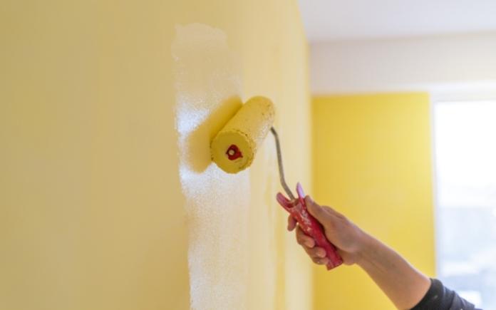Hand rolling yellow paint on a wall