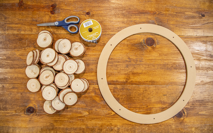 Materials to make a wood round wreath, including ribbon, scissors, floral wreath ring and wood rounds.