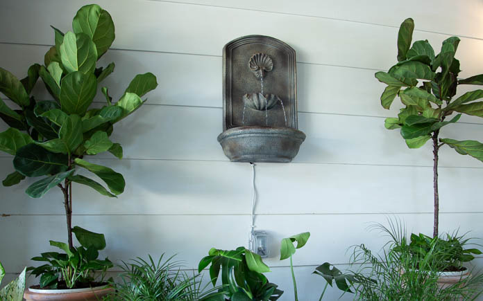 Outdoor wall fountain on the siding of a home's exterior next to green leafy plants