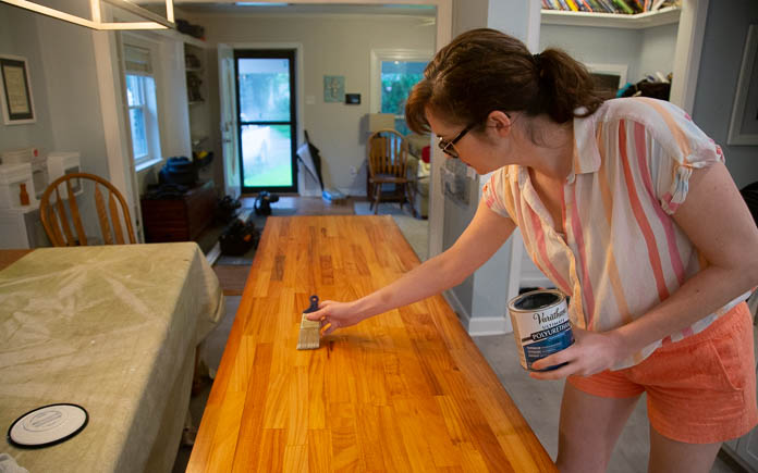Lindsey Binion brushes polyurethane onto a butcher block countertop