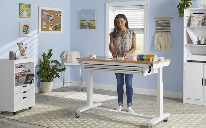 Woman working at a Husky Adjustable Height Solid Wood Top Workbench Table in White in a craft room