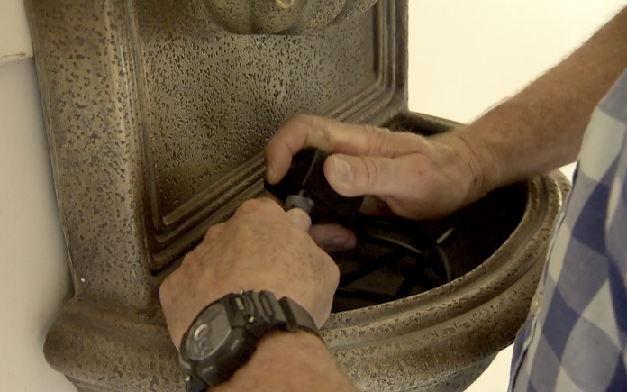 Hands plugging in a pump to a wall fountain