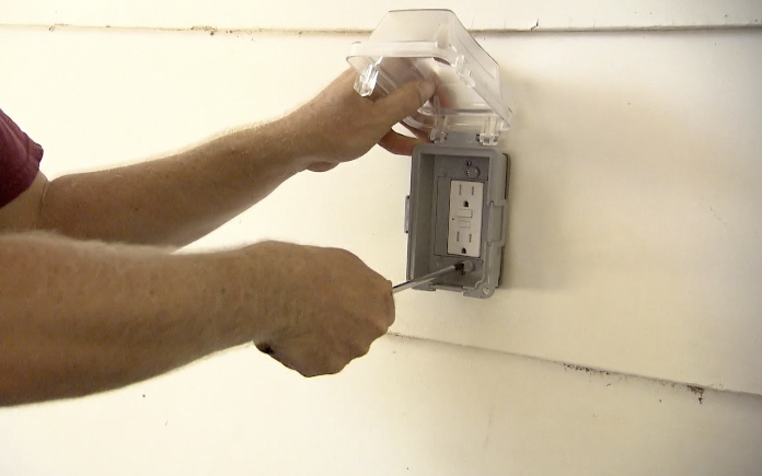 Using a screwdriver to secure a GFCI outlet to a home's exterior