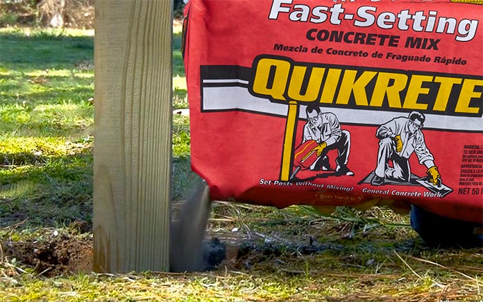 Quikrete fast-setting concrete in the red bag pouring into a fence post hole