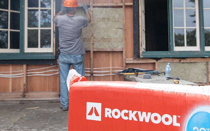 Rockwool stone wool insulation package in foreground with construction worker installing insulation batt on home's exterior in background