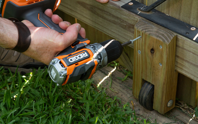 Ridgid drill drilling galvanized screws into a caster wheel on a fence gate