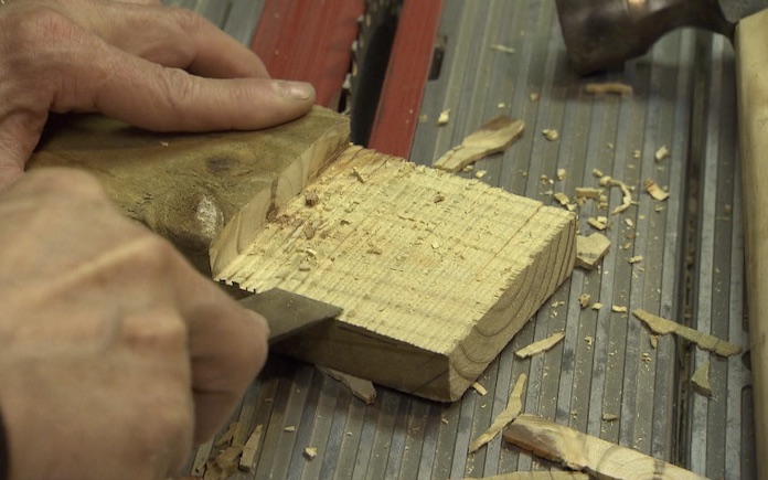 Hand using a wood scraper to smooth a notch out of a two-by-four pressure-treated board