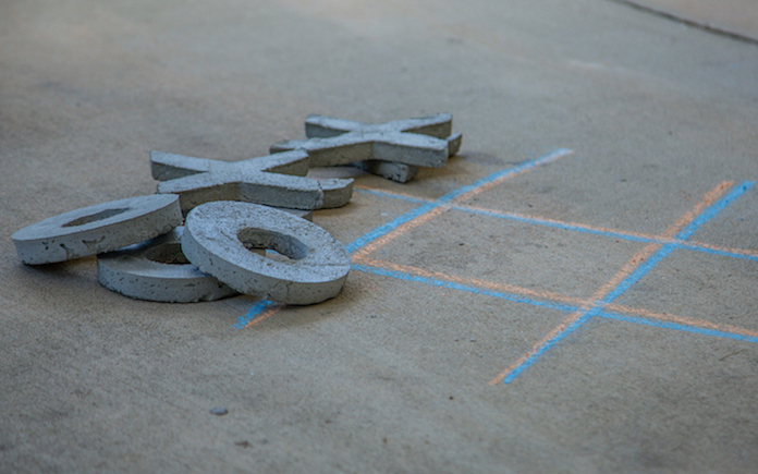 Concrete tic-tac-toe pieces next to chalk-drawn board