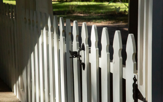 White picket fence with a gate and black latch next to a carport