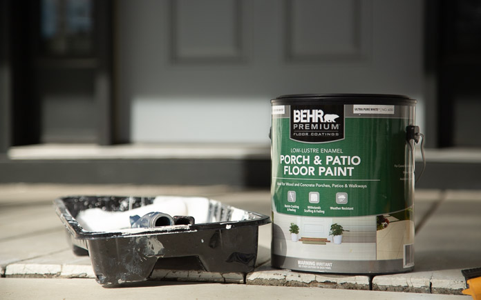 Behr Premium Porch and Patio Floor Paint next to a paint tray resting on front porch deck boards
