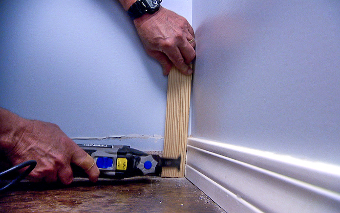 Hands using an oscillating saw to trim a baseboard to accommodate a batten for a board and batten wall