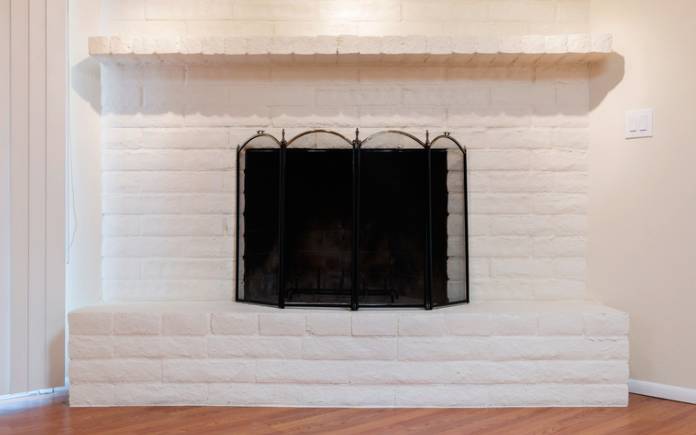 White painted brick fireplace with black screen and hardwood floor