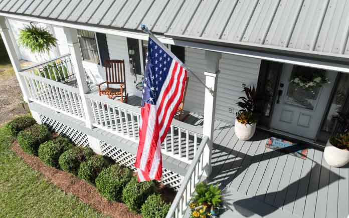 Overhead view of a front porch with gray deck boards and handrail tops with an American flag flying from a post.