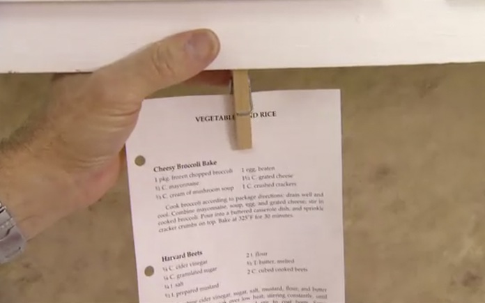 Printed recipe hanging from a clothespin attached to the underside of a cabinet