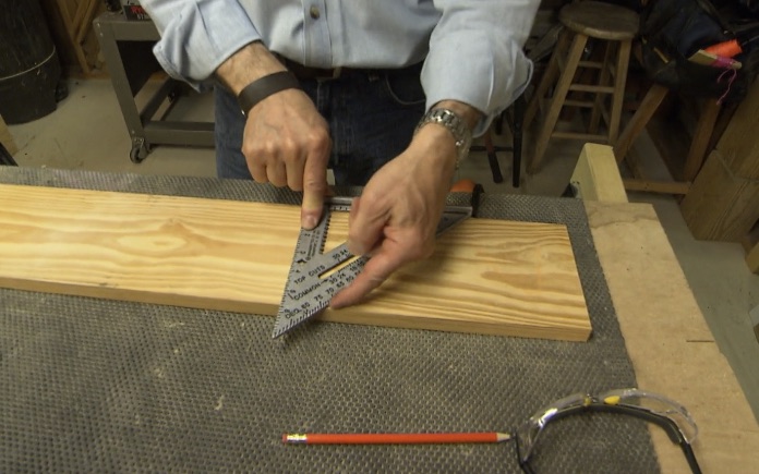 Hands placing a speed square on a piece of lumber on a work table.