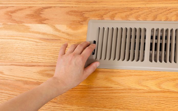 Hand opening up a floor vent heater on oak floor