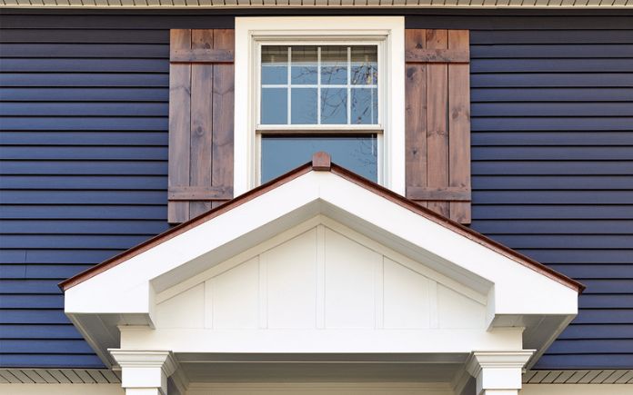 Window with wood shutters above a gable on a home with dark siding