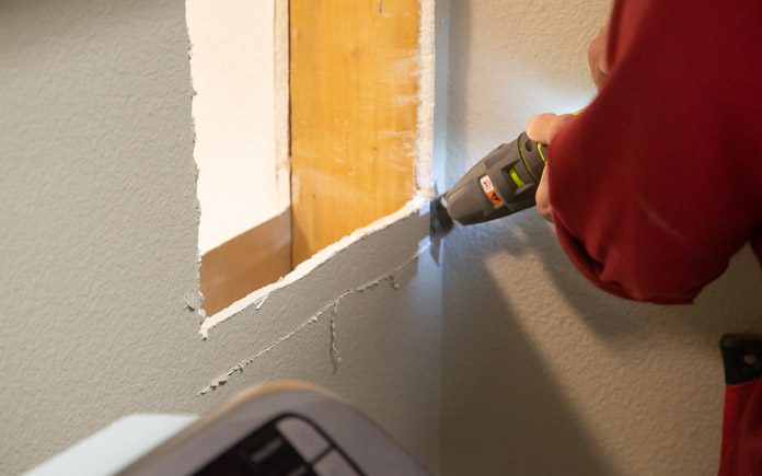 Hands using an oscillating saw to cut a hole in drywall