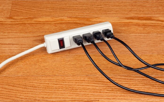 Electrical power strip with black cords plugged in on a wood floor